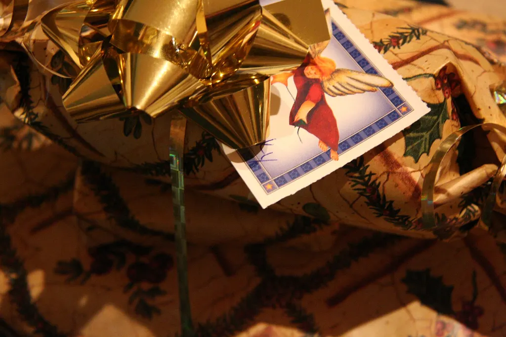 A gift wrapped in Christmas paper with a gold ribbon bow and a gift tag